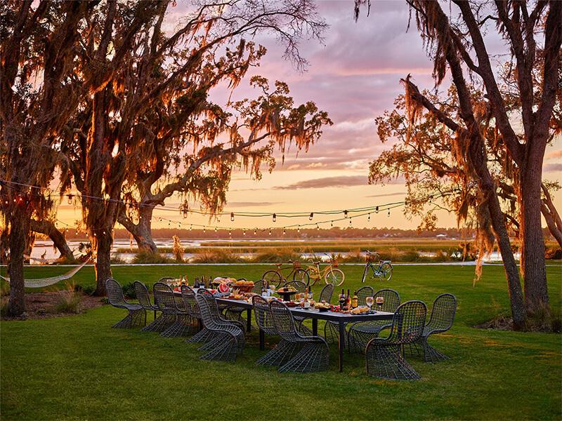 Sunset at a backyard party near a waterway featuring Universal's Del Mar Dining Chair and long, rectangular dining table.